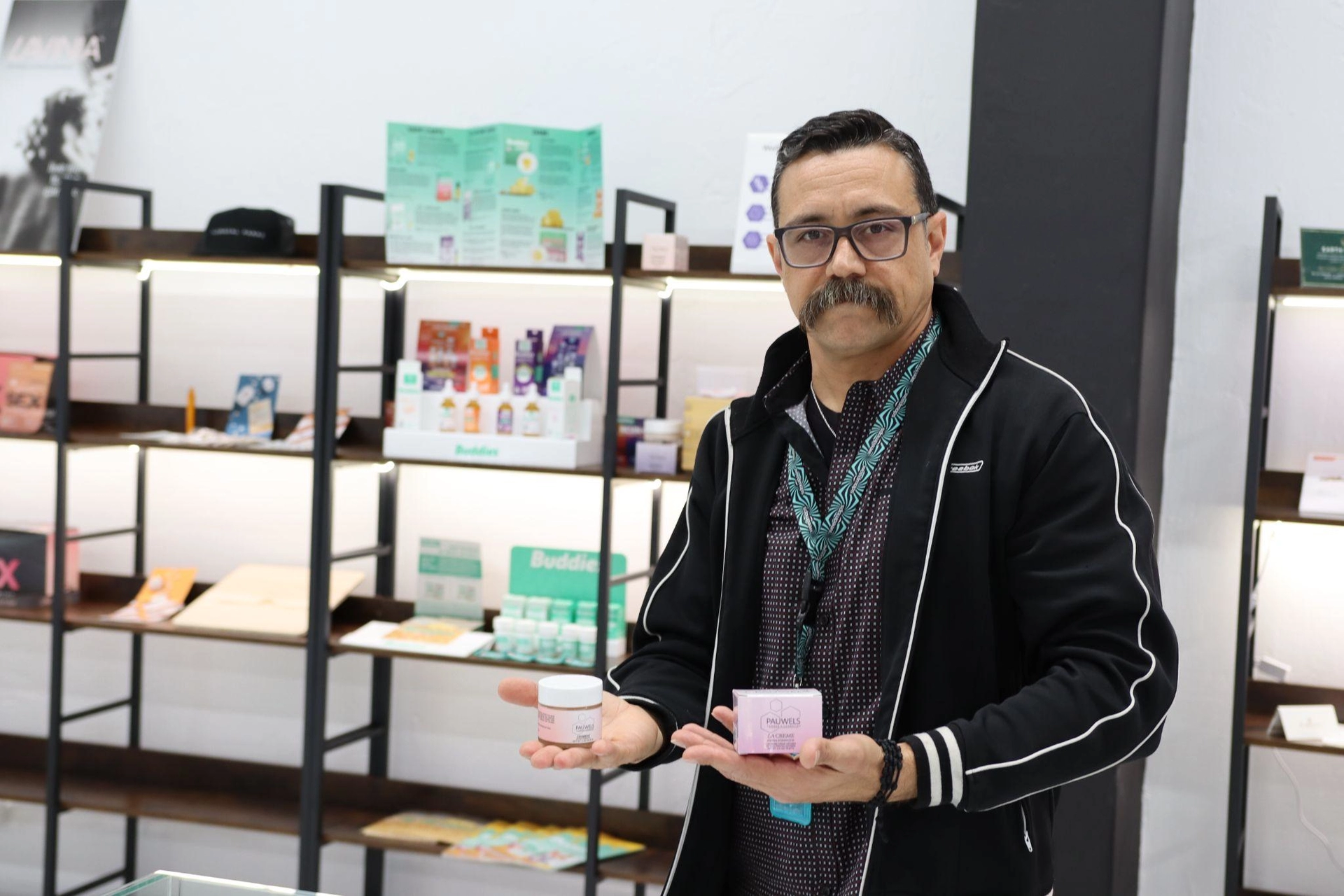 Image of man holding up products as he stands before shelving with merchandise