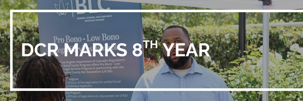 DCR Marks 8th Year, Graphic: photo of man in front of a banner and speaking to another individual